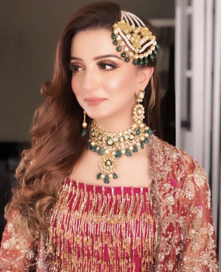 a woman wearing a red and gold outfit with jewelry on her head, posing for the camera