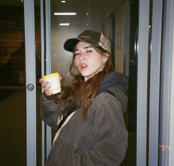 a young woman holding a cup in her right hand and wearing a hat on top of her head