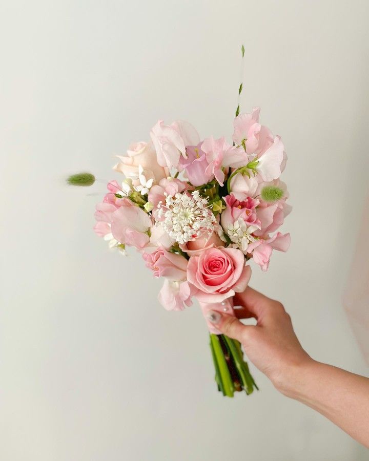 a person holding a bouquet of pink flowers in their left hand, with white background