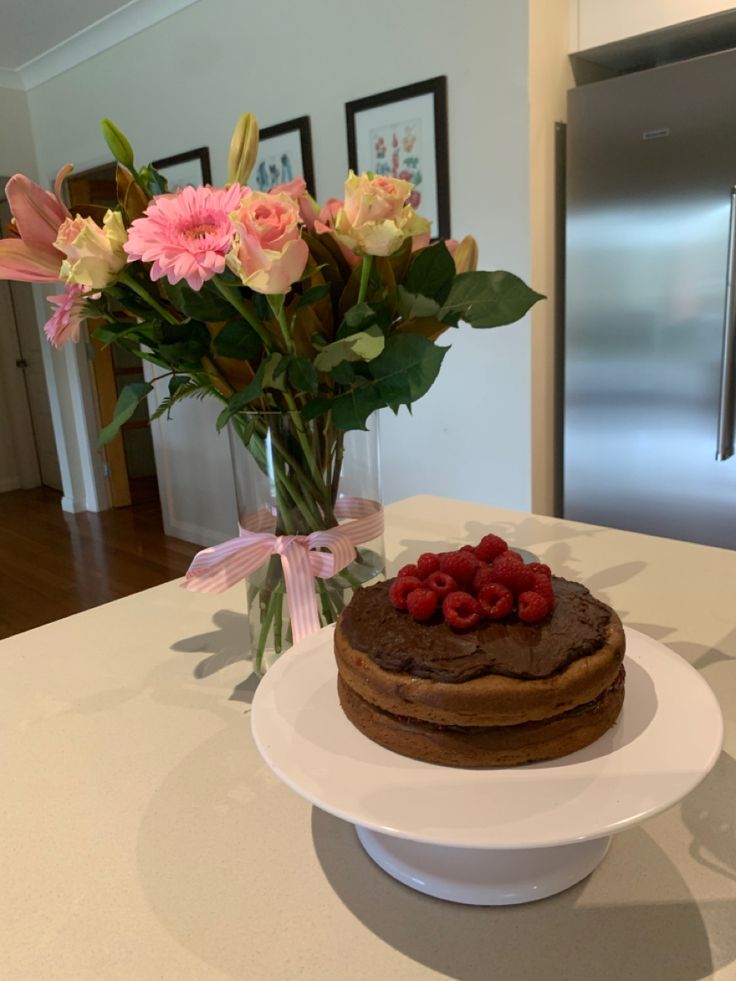 a chocolate cake with raspberries and flowers in a vase on a counter top