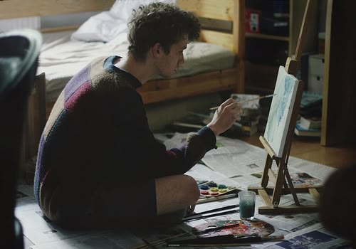 a man sitting in front of a easel painting