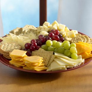 a red plate filled with cheese, crackers and grapes on top of a wooden table