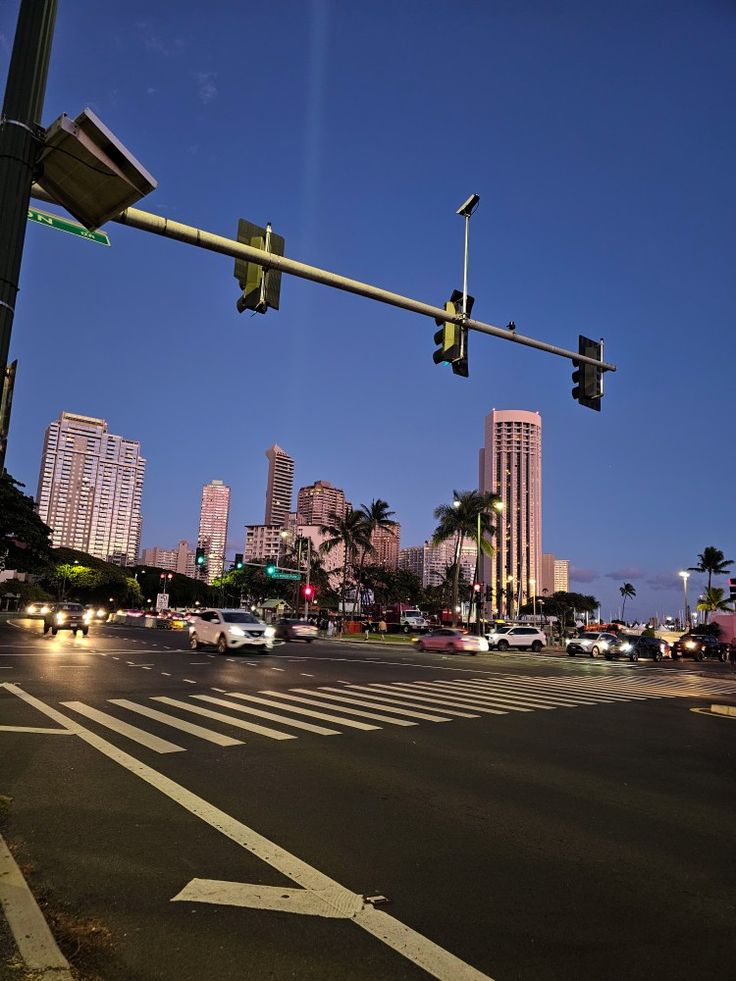 an intersection with traffic lights and palm trees in the background at dusk, near a city