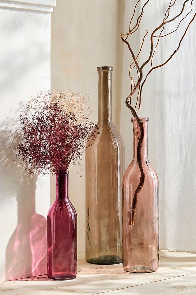 three vases with dried flowers in them sitting on a shelf next to a window