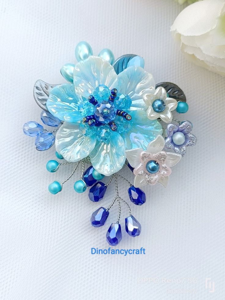 a blue and white flower brooch sitting on top of a table next to flowers