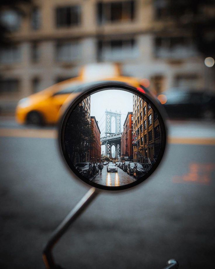 a side view mirror on the handlebars of a motor scooter in front of a city street