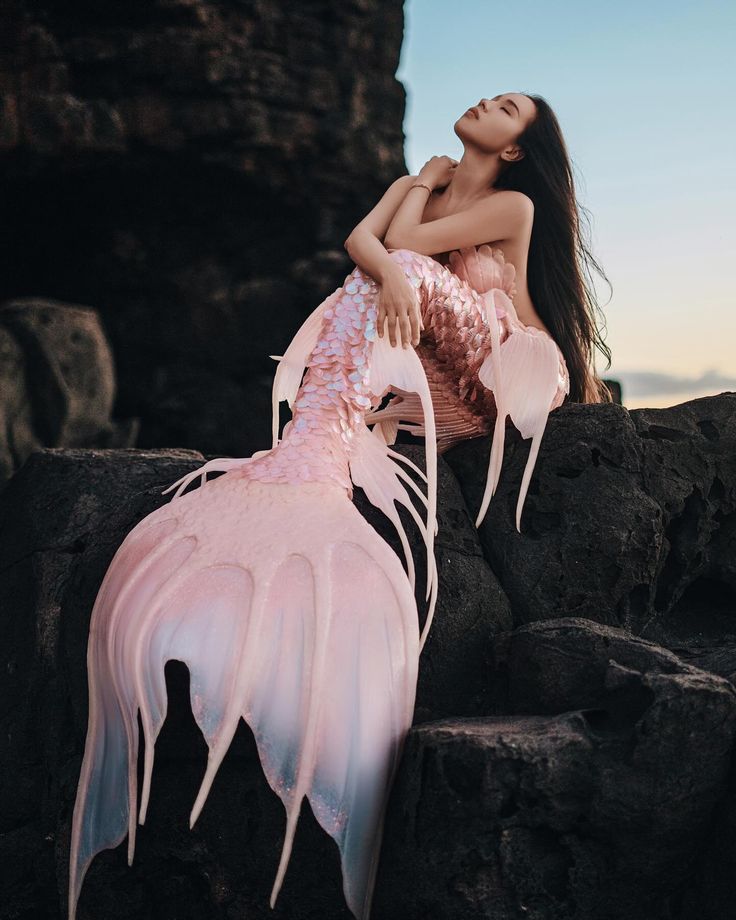 a woman sitting on top of a rock next to a large pink feathered animal