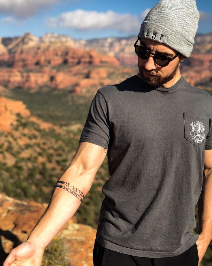 a man in sunglasses and a hat is holding his hand out to the side while standing on top of a mountain