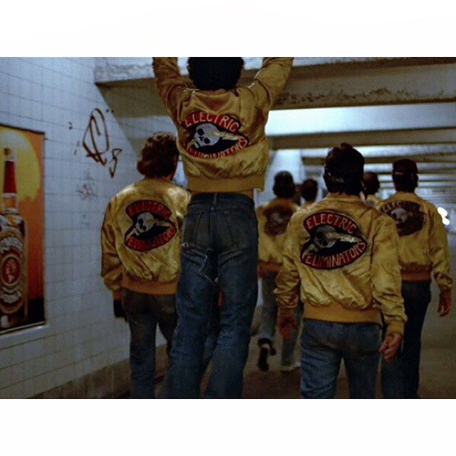 a group of people wearing jackets and jeans walking down a hallway with their hands in the air