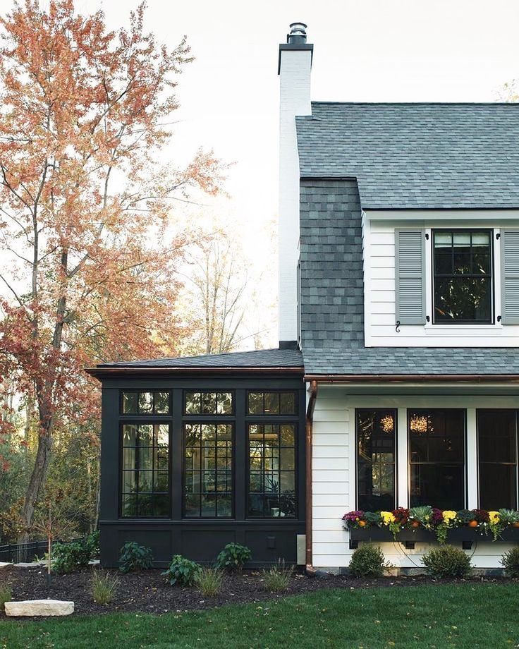 a white house with black shingles and flowers in the window boxes on the front