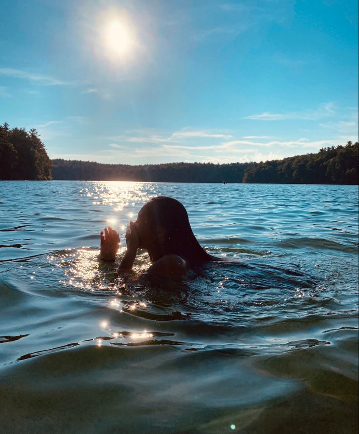 a person swimming in the water with their head above the water's surface and trees behind them