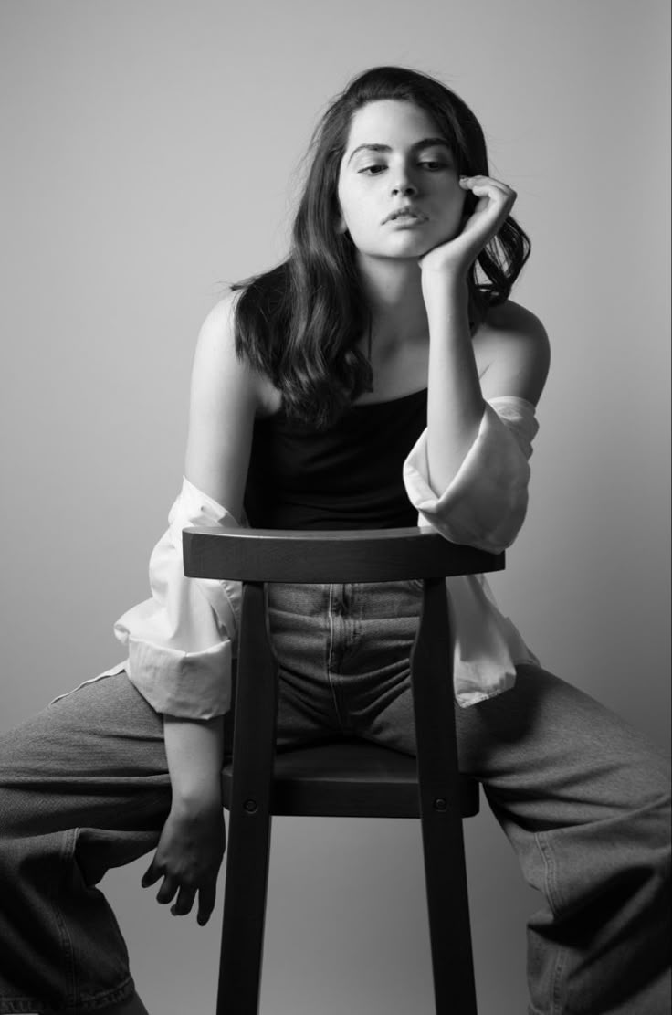 a woman sitting in a chair with her hand on her head and looking at the camera