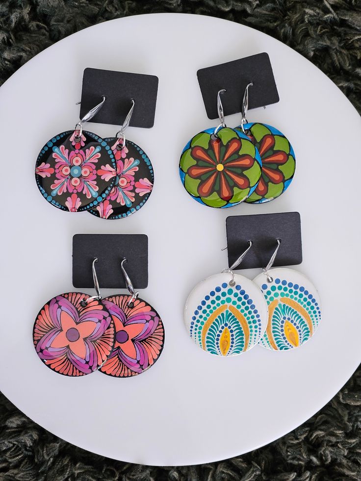 four pairs of earrings are on a white plate with black tags hanging from it's sides