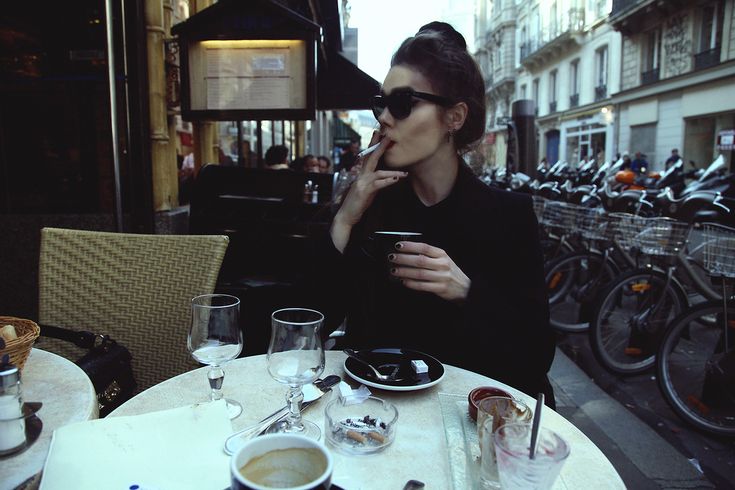 a woman sitting at an outdoor table using her cell phone while eating food and drinking coffee