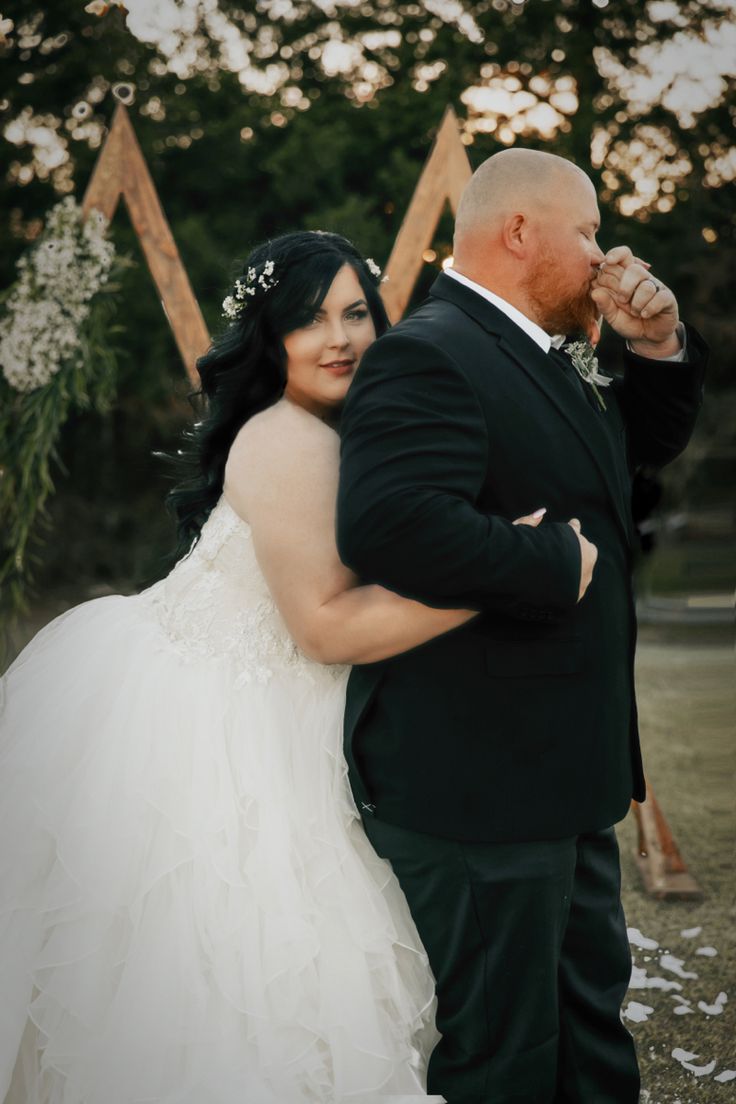 a bride and groom standing in front of a wedding arch with white flowers on it