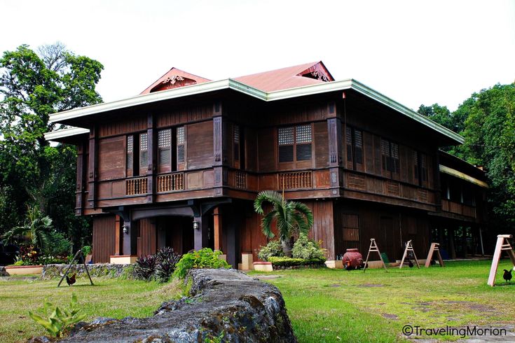 a large wooden house sitting in the middle of a lush green field next to trees