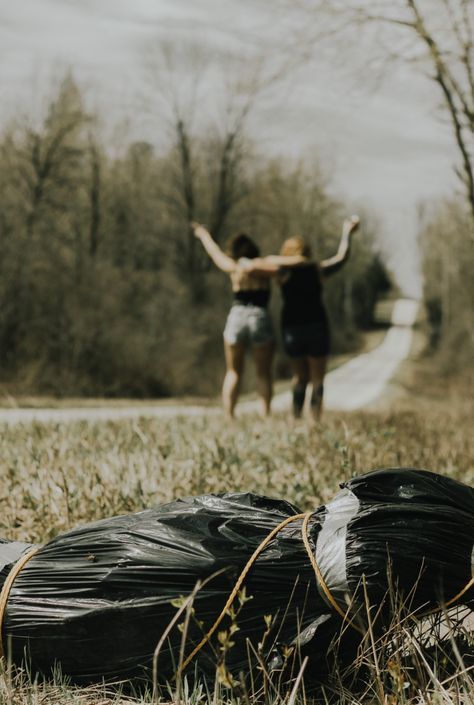 two people are walking in the grass near trash bags and an old bag on the ground