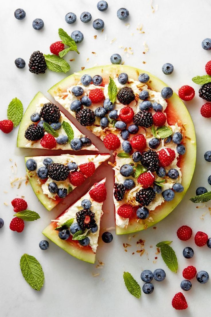 a fruit pizza with berries, blueberries, raspberries and mint leaves on it