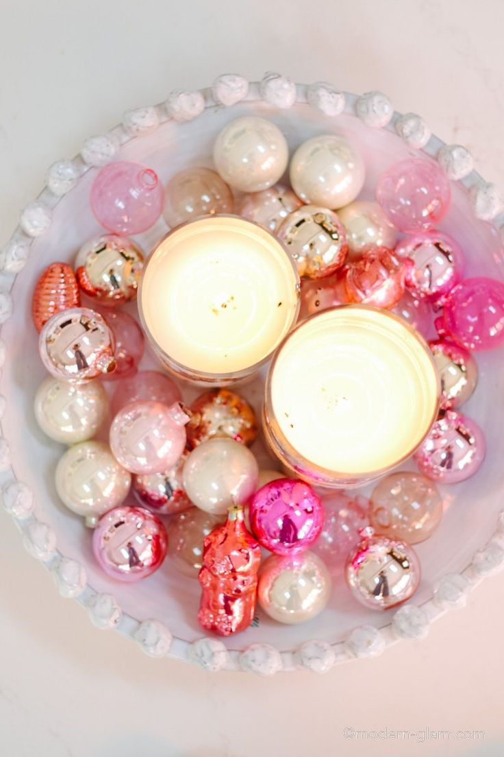 a bowl filled with lots of different types of ornaments on top of a table next to a candle