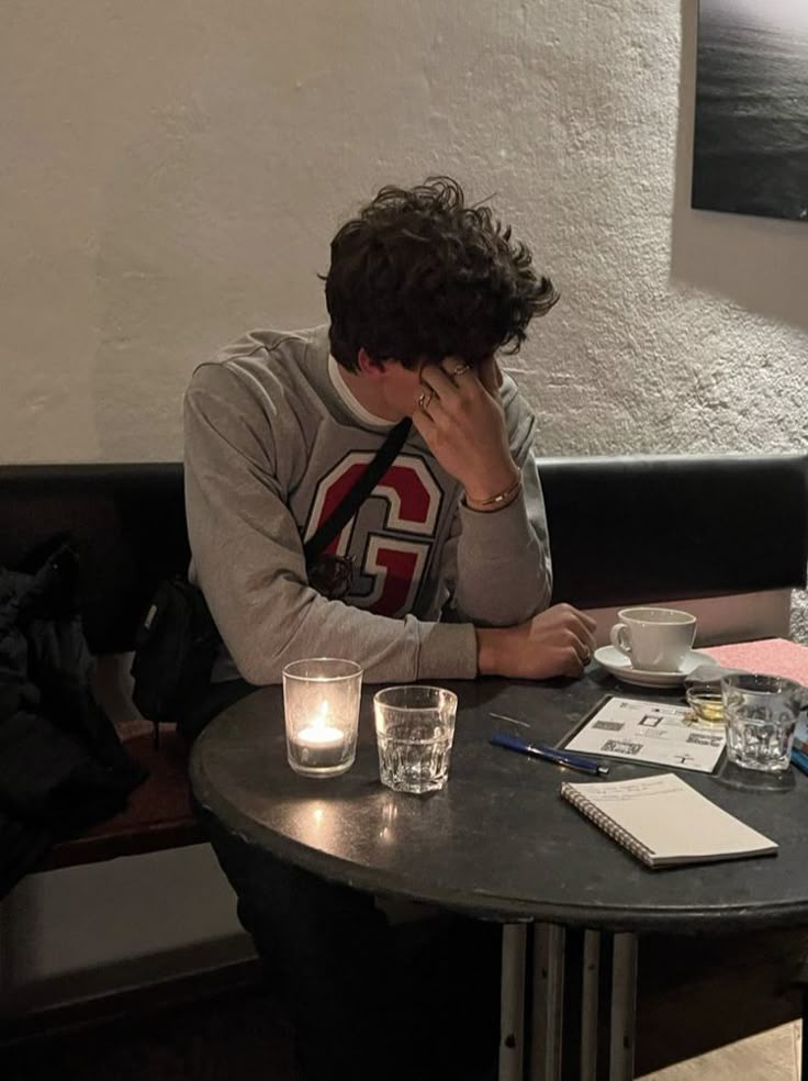 a man sitting at a table with his head in his hands and writing on a notebook