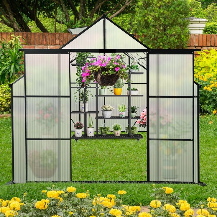 a small greenhouse with flowers in it on the grass near some bushes and yellow flowers