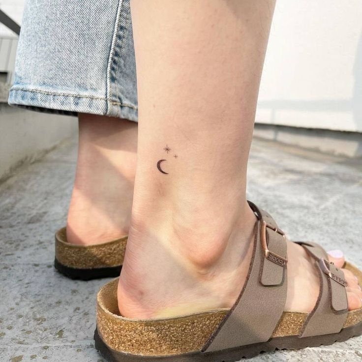 a woman's foot with a small crescent tattoo on her left ankle, next to a pair of jeans