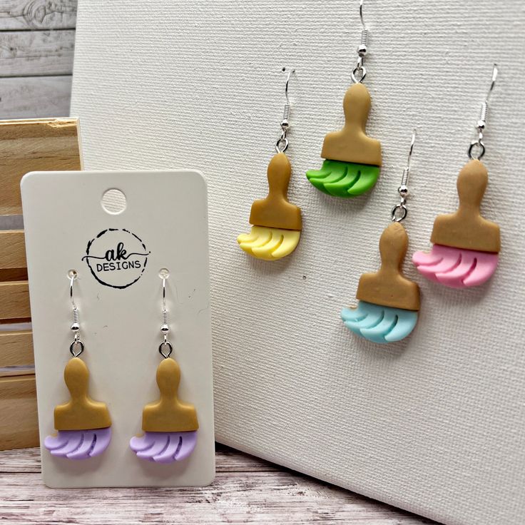 three pairs of earrings with different colors and shapes hanging from hooks on a white background