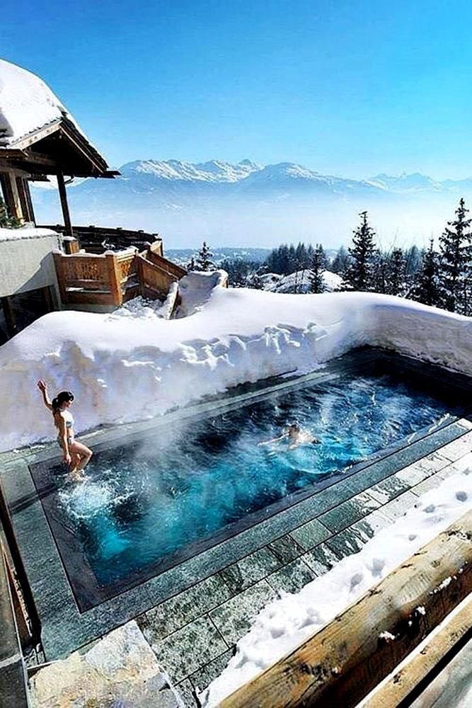 an outdoor hot tub with snow on the ground and people swimming in it, surrounded by mountains