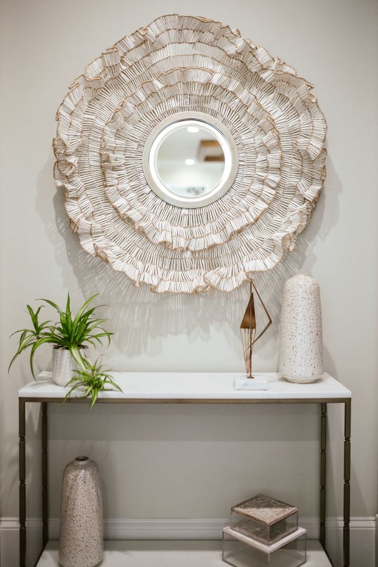 a white table with a mirror and vases on it next to a wall mounted plant