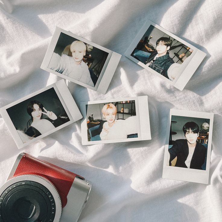 four polaroid photos are laying on a bed with white sheets and a red camera