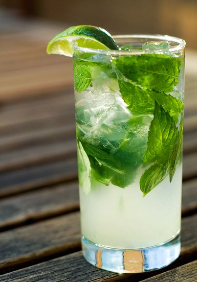 a glass filled with ice and mint on top of a wooden table next to a slice of lime