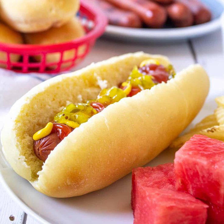 hot dog buns on a plate with watermelon and other food items in the background