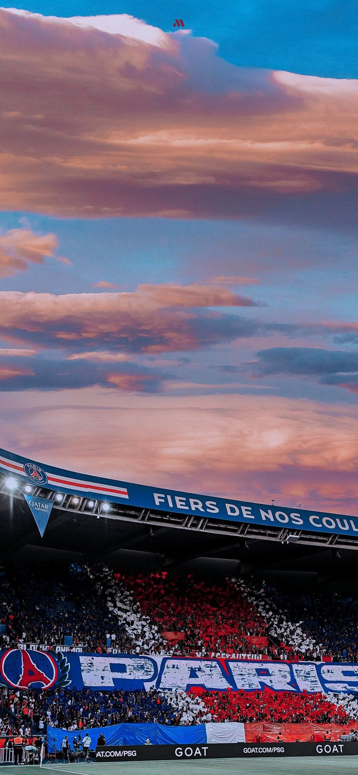 a stadium filled with lots of people under a cloudy blue and pink sky at sunset