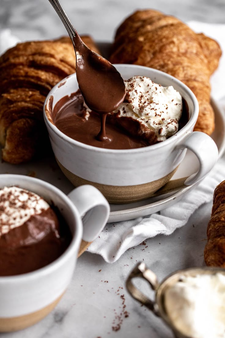 there is a spoon that is in the bowl with some ice cream on it and croissants behind it