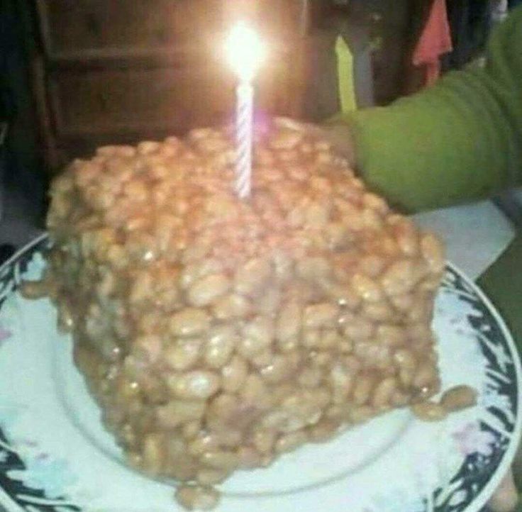 a birthday cake with a single lit candle on it and peanuts all over the top