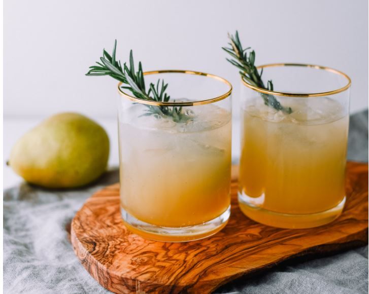 two glasses filled with lemonade sitting on top of a wooden tray next to a pear