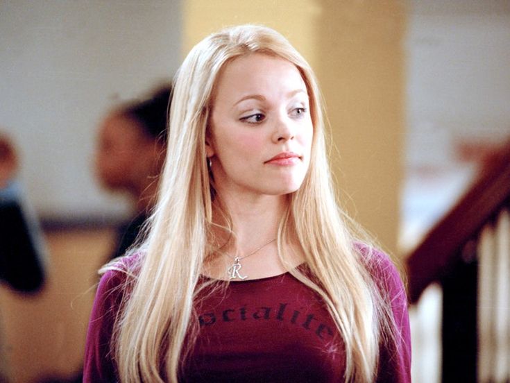 a woman with long blonde hair is standing in front of stairs and looking off into the distance