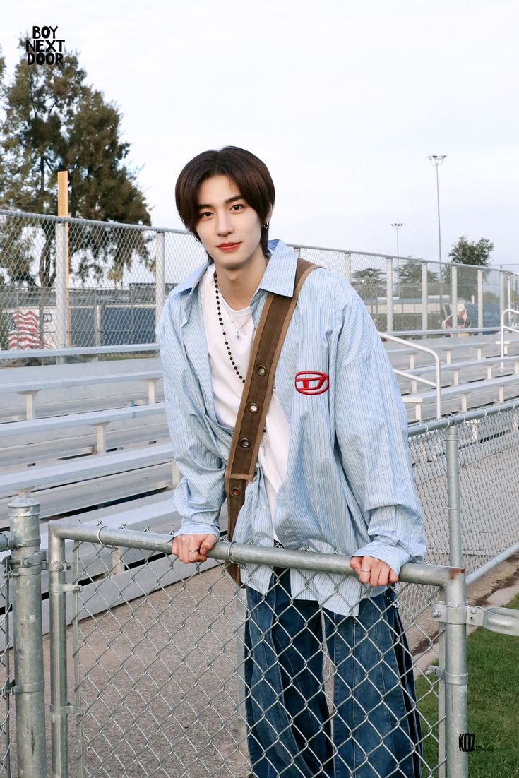 a young man standing behind a fence with his hands on his hips and looking at the camera