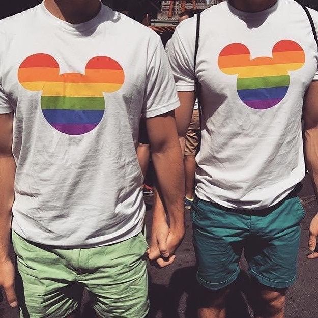 two men wearing mickey mouse shirts with rainbow colors on their chest and one man holding the other's hand