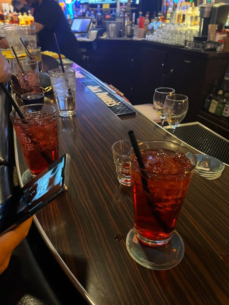 people sitting at a bar with drinks in front of them and cell phones on the counter