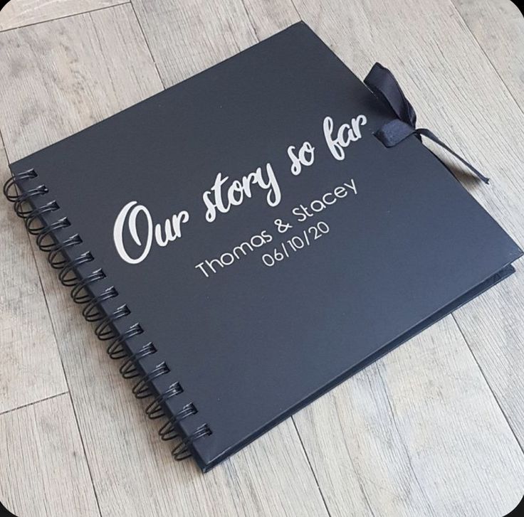 a black wedding guest book with the words our story so far on it and a bow