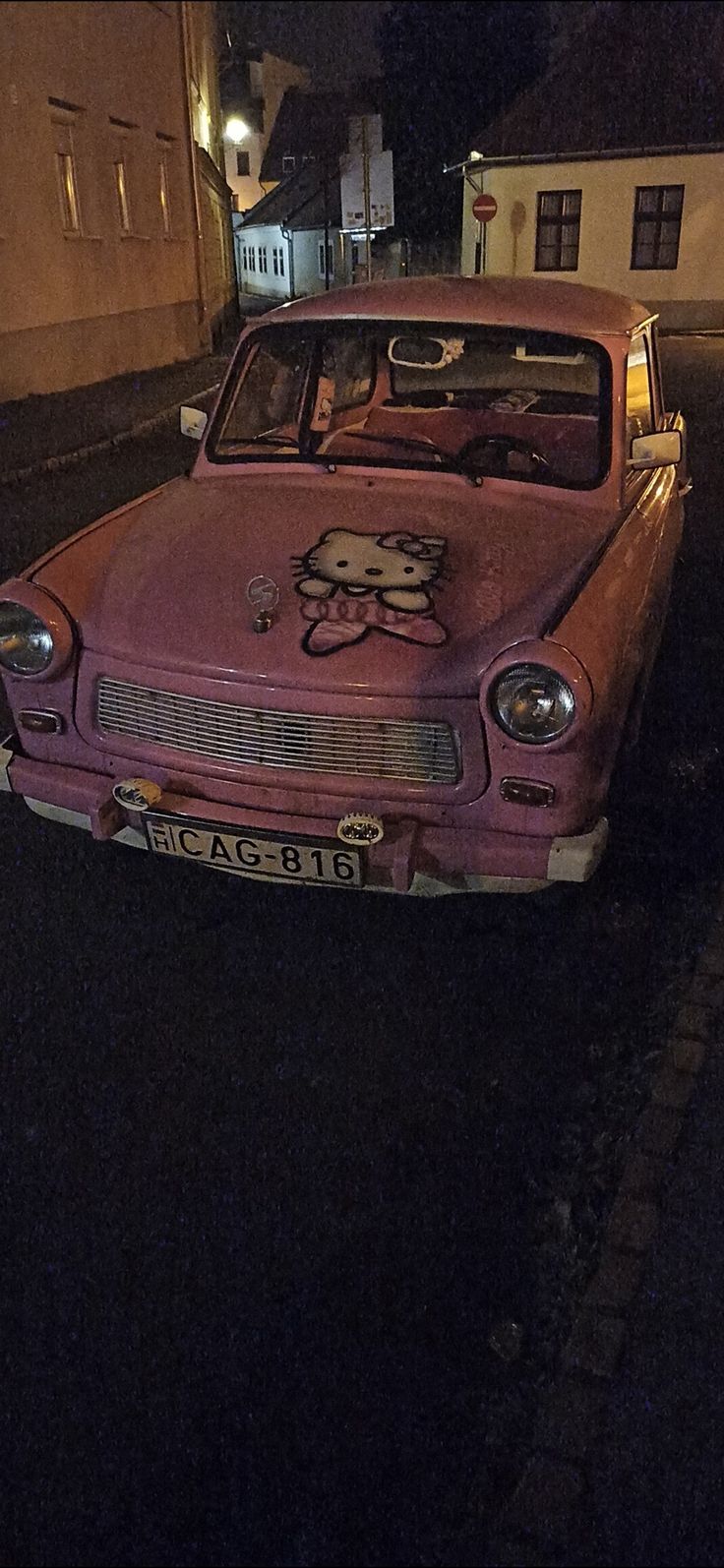 an old pink car with a hello kitty on it's hood parked in the street