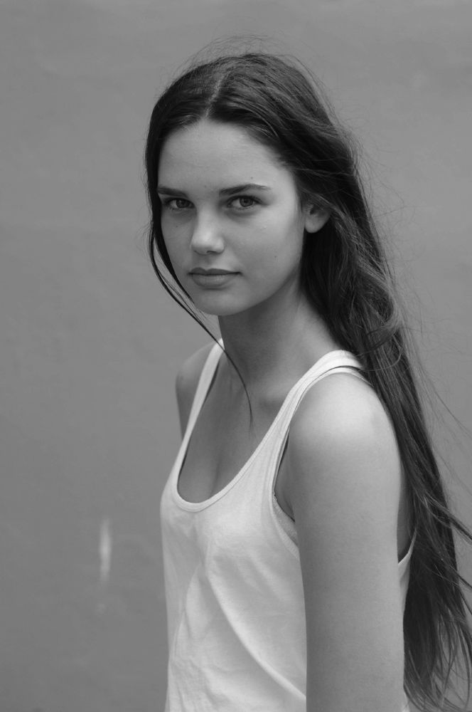 a young woman with long hair standing in front of a wall wearing a tank top