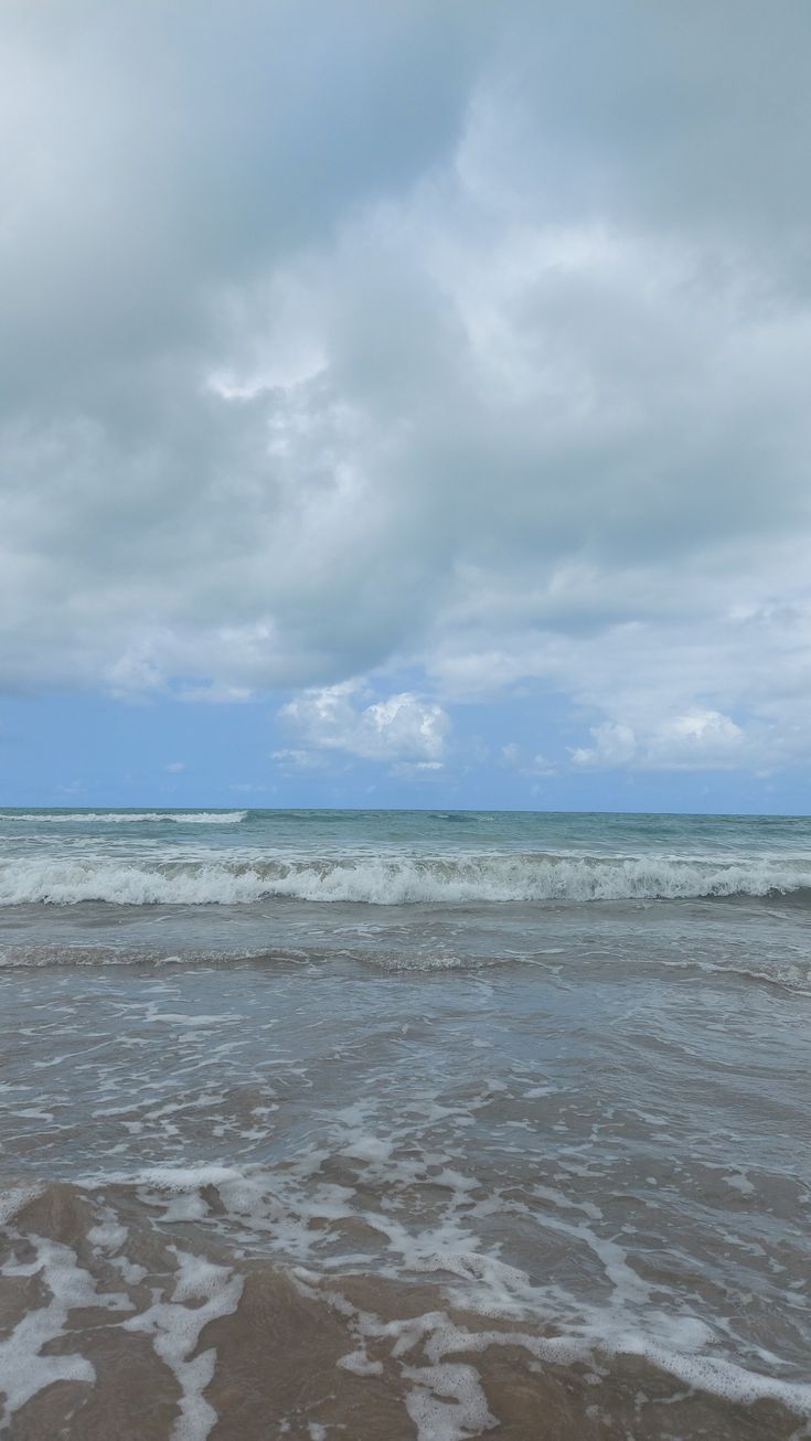 an ocean view with waves coming in to shore and the sky is filled with white clouds