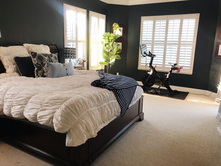 a large bed sitting inside of a bedroom next to two windows with shutters on them