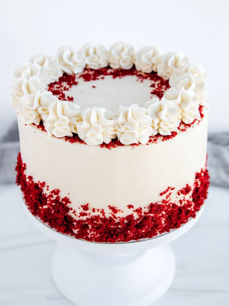 a red velvet cake with white frosting and sprinkles on a pedestal