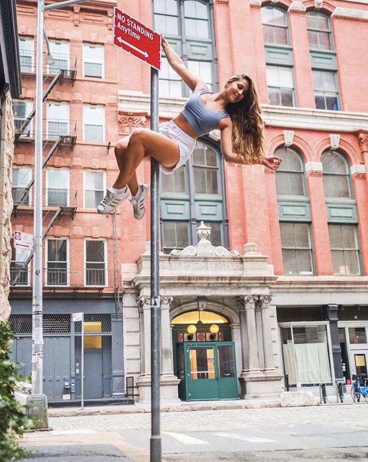 a woman standing on top of a pole next to a street sign and buildings in the background