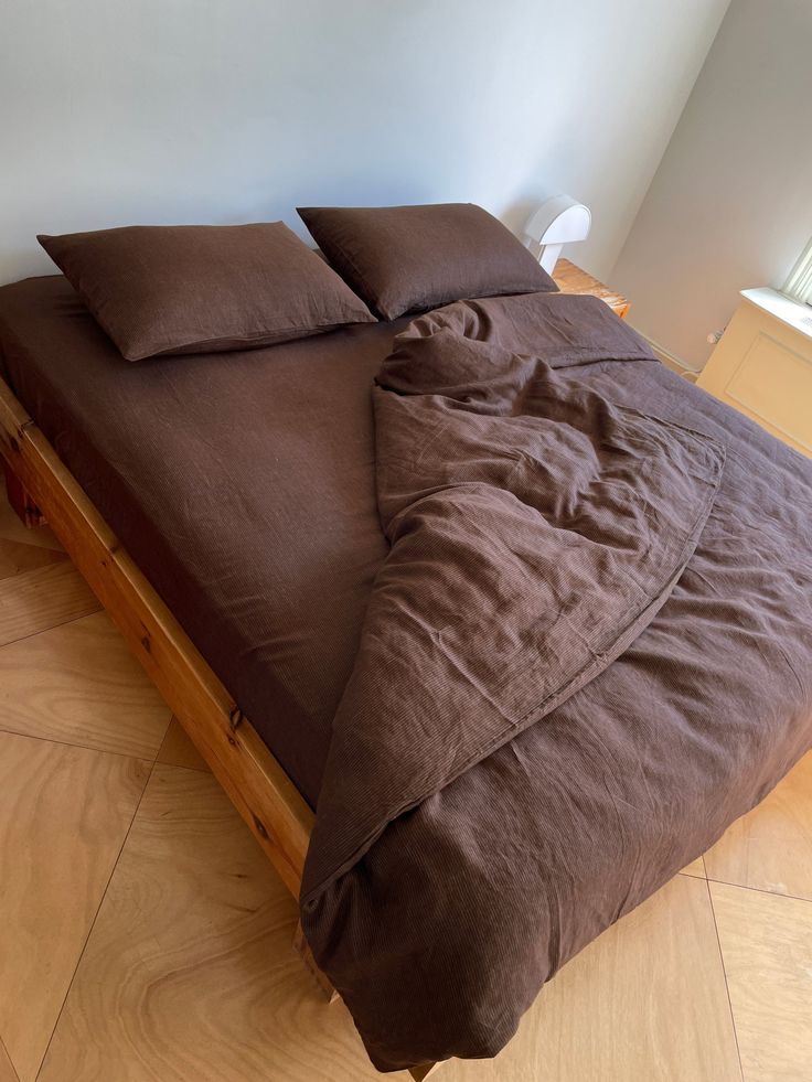 a bed with brown sheets and pillows on top of it in a room that has wood flooring