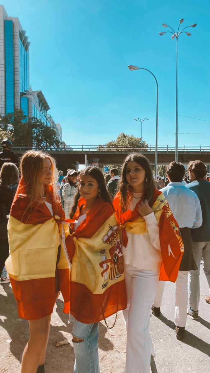 two women standing next to each other in front of a group of people on the street