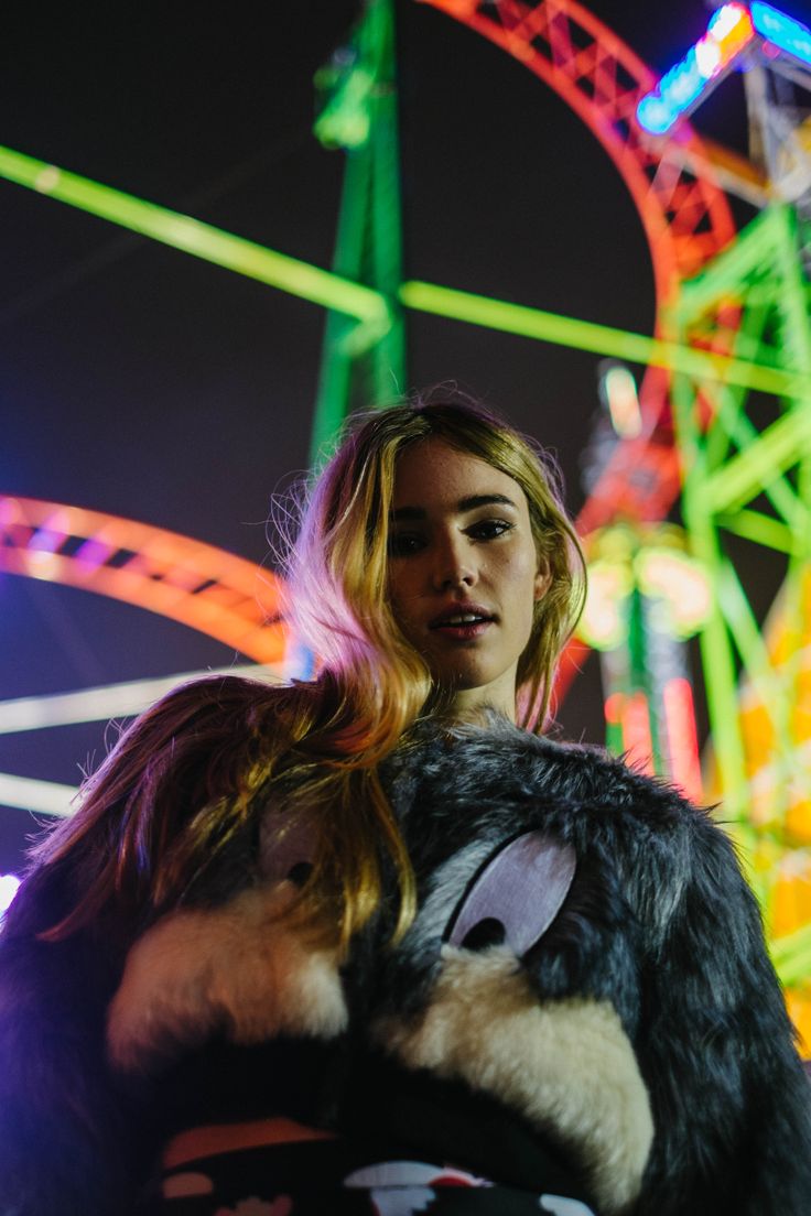 a woman standing in front of a carnival ride at night with her arms around the shoulders